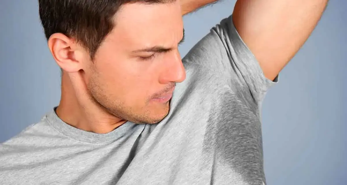 Un homme sent ses aisselles moites, cherchant comment enlever les taches sous les aisselles.