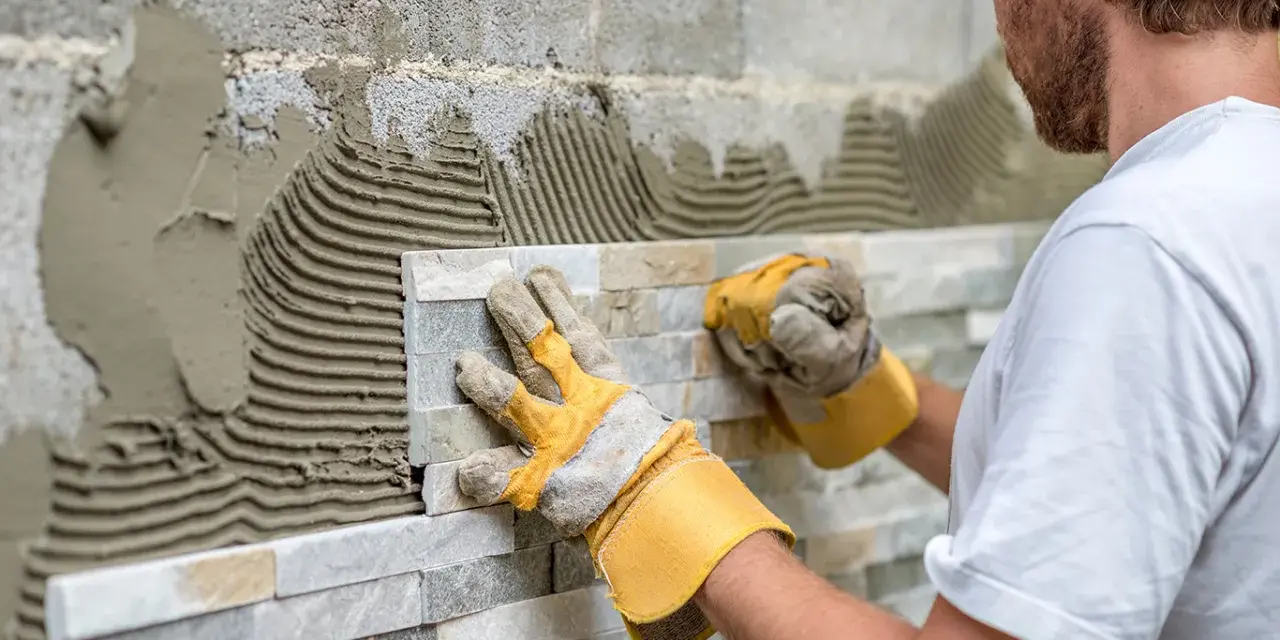 Pose de pierre de parement en quinconce. Un artisan pose des pierres naturelles sur un mur avec du mortier.