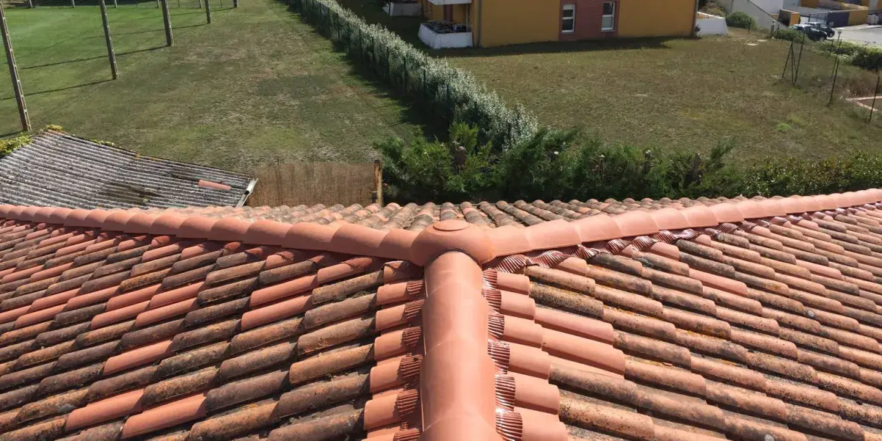 Vue aérienne d'un toit en tuiles rouges, avec des bâtiments et de la verdure en arrière-plan. Faut-il imperméabiliser les tuiles pour les protéger ?