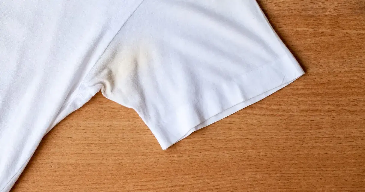 T-shirt blanc avec une tache de transpiration incrustée sous le bras, sur fond de bois.