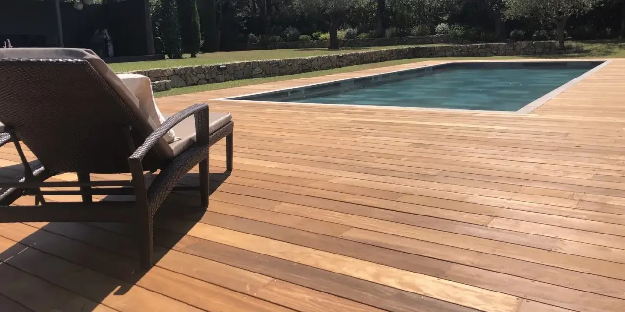 Terrasse en bois d'Ipe, baignée de soleil, avec une chaise longue invitant à la détente près de la piscine.
