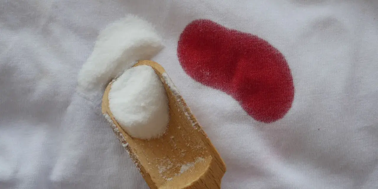 Poudre blanche sur tissu blanc à côté d'une tache rouge. Astuce pour savoir comment enlever des taches de sang sur du coton.