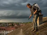 Un homme traite un toit couvert de mousse, sous un ciel orageux. Il se demande combien de temps avant pluie son anti-mousse sera efficace.