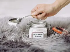 Une main tient une cuillère de bicarbonate de soude au-dessus d'un tapis moelleux. Le bicarbonate de soude est un produit naturel et polyvalent pour le nettoyage.