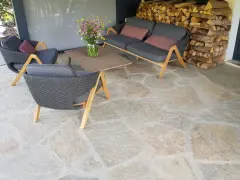 Terrasse en pierre naturelle extérieure, protégée par un imperméabilisant, avec mobilier de jardin confortable et un bouquet de fleurs sauvages.