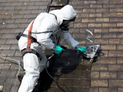 Nettoyage d'un toit en fibro ciment avec un appareil de nettoyage sous pression, l'opérateur porte une combinaison de protection et un masque.