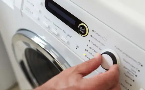 Main d'une personne réglant la température de lavage d'une couette sur un panneau de commande de machine à laver.