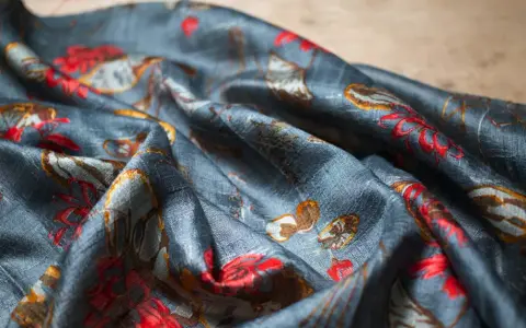 Tissu de soie bleu nuit avec un motif de fleurs rouges et de feuilles dorées. Une tache de gras sur soie, subtile, se fond dans le motif.