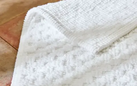 Un tapis de bain blanc moelleux, avec un motif texturé, est posé sur un sol en terre cuite. Il est temps de se demander a combien laver un tapis de bain pour qu'il reste ainsi.
