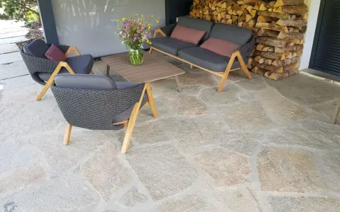 Terrasse en pierre naturelle extérieure, protégée par un imperméabilisant, avec mobilier de jardin confortable et un bouquet de fleurs sauvages.