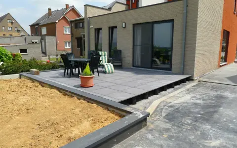 Une terrasse moderne avec un dallage gris sur plots, prête pour un couler dalle. Mobilier de jardin et végétation environnante.