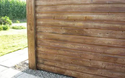 Bardage en bois de mélèze, traité pour l'extérieur, avec un poteau vertical. Le bois présente des nœuds et un grain prononcé.