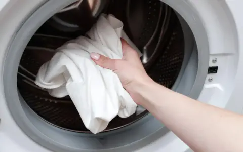 Main tenant met une serviette blanche dans le tambour d'une machine à laver pour dissoudre lessive durcie.