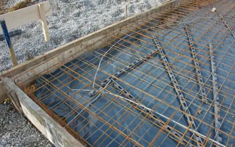 Préparation pour couler une dalle béton : film plastique, treillis métallique et coffrage en bois. On ne coule pas une dalle béton directement sur la terre.