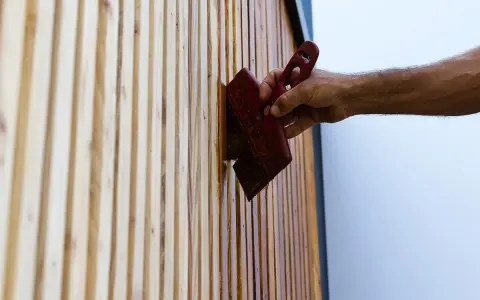 Maintenir son bois en parfait état : une main applique une huile protectrice sur des lattes de bois, comme pour fabriquer son huile de teck.