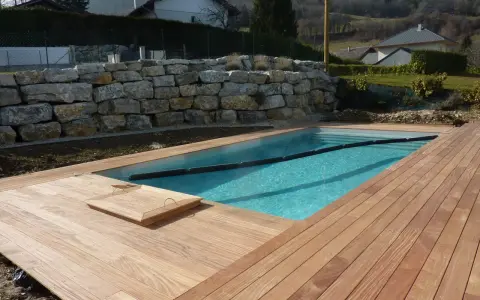 Piscine en bois avec terrasse en bois, mur de soutènement en pierre. Entretien piscine bois facile avec cette belle installation.