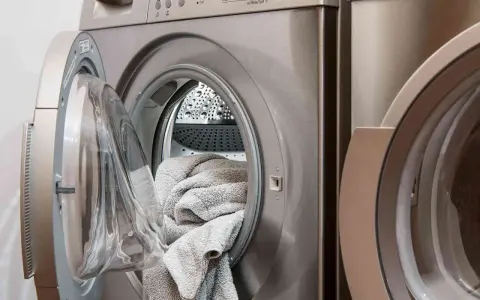Machine à laver avec une porte ouverte, remplie de linge gris. Choisir la lessive la moins toxique pour un lavage sain.