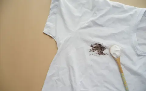 Tache sur t-shirt blanc après lavage, avec une cuillère de poudre blanche à côté.