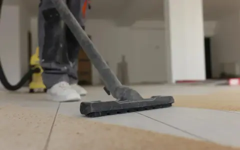 Un aspirateur en action pour enlever l'enduit sur le carrelage. La poussière est aspirée, laissant le sol propre.