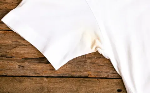 T-shirt blanc avec une tache jaune sous l'aisselle, sur un fond de bois rustique.
