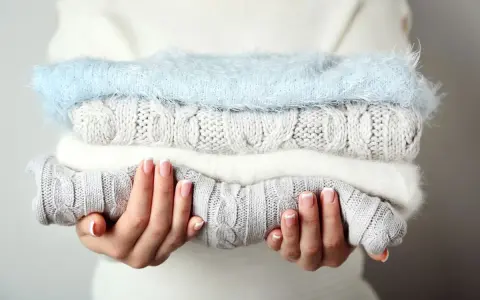 Pile de pulls en laine douce, gris et blanc, avec un pull bleu ciel. Idéal pour savoir comment detacher un pull blanc et le garder comme neuf.