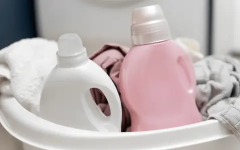 Deux bouteilles de lessive, une blanche et une rose, dans un panier avec du linge.