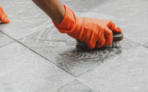 Main tenant, ganté, frotte le sol carrelé avec une brosse pour nettoyer le ciment sec.