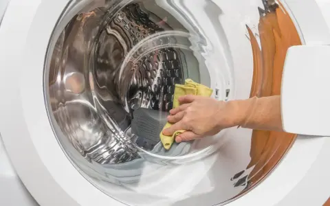 Main d'une personne utilisant un chiffon jaune pour nettoyer l'intérieur d'une machine à laver, une méthode naturelle pour nettoyer machine a laver vinaigre.