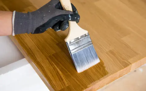 Main tenant avec un pinceau pour enlever l'huile de lin sur du bois.
