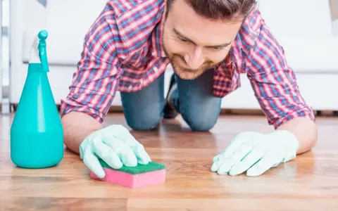 Un homme, muni de gants et d'une éponge, s'agenouille pour nettoyer une tache sur le parquet.