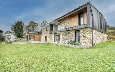 Une maison en pierre rénovée, mêlant tradition et modernité avec des touches de bois et de métal. Un jardin verdoyant entoure cette demeure.