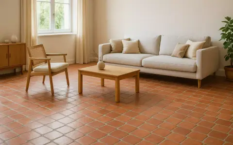 Un salon cosy avec un canapé clair, un fauteuil en rotin et un sol en **sol tomette ancienne** réchauffant l'atmosphère.