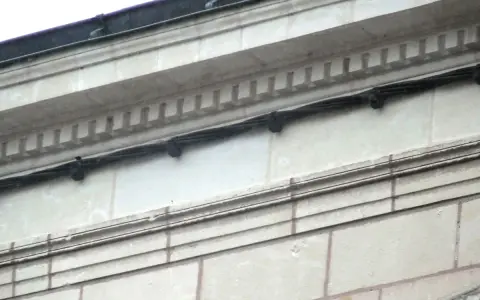 Détail d'une façade en tuffeau avec des câbles noirs fixés. L'image montre comment poncer du tuffeau pour restaurer sa surface.