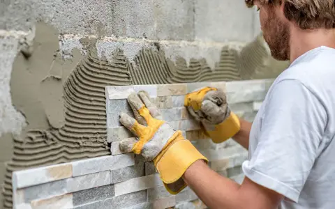 Pose de pierre de parement en quinconce. Un artisan pose des pierres naturelles sur un mur avec du mortier.