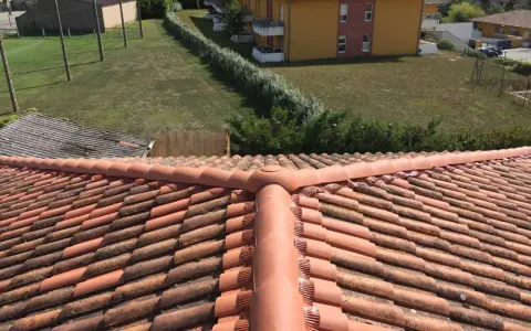 Vue aérienne d'un toit en tuiles rouges, avec des bâtiments et de la verdure en arrière-plan. Faut-il imperméabiliser les tuiles pour les protéger ?