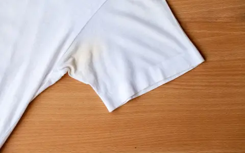 T-shirt blanc avec une tache de transpiration incrustée sous le bras, sur fond de bois.
