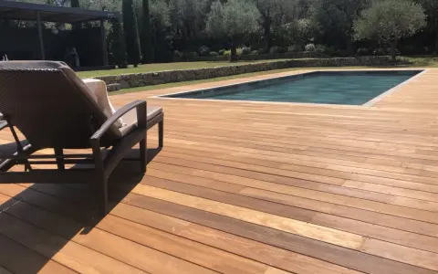 Terrasse en bois d'Ipe, baignée de soleil, avec une chaise longue invitant à la détente près de la piscine.