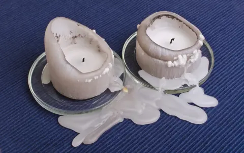 Deux bougies fondent, laissant une tache de bougie sur la pierre poreuse. La cire blanche coule sur les soucoupes en verre.