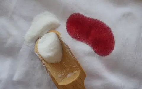 Poudre blanche sur tissu blanc à côté d'une tache rouge. Astuce pour savoir comment enlever des taches de sang sur du coton.