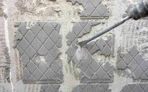 Outil pneumatique en action pour enlever ciment colle sur carrelage. Poussière et débris volent.