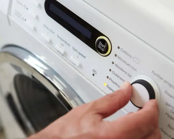 Main d'une personne réglant la température de lavage d'une couette sur un panneau de commande de machine à laver.
