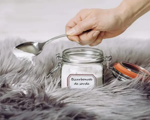 Une main tient une cuillère de bicarbonate de soude au-dessus d'un tapis moelleux. Le bicarbonate de soude est un produit naturel et polyvalent pour le nettoyage.