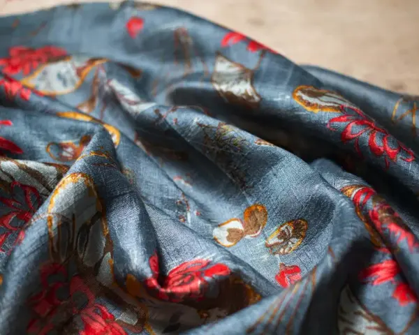 Tissu de soie bleu nuit avec un motif de fleurs rouges et de feuilles dorées. Une tache de gras sur soie, subtile, se fond dans le motif.