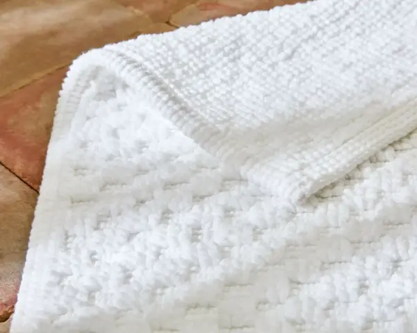Un tapis de bain blanc moelleux, avec un motif texturé, est posé sur un sol en terre cuite. Il est temps de se demander a combien laver un tapis de bain pour qu'il reste ainsi.