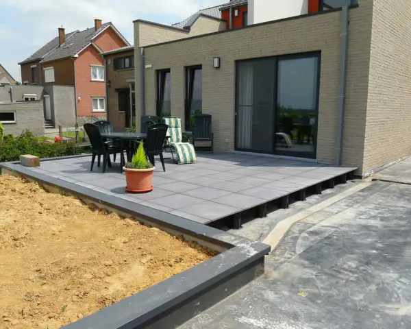 Une terrasse moderne avec un dallage gris sur plots, prête pour un couler dalle. Mobilier de jardin et végétation environnante.