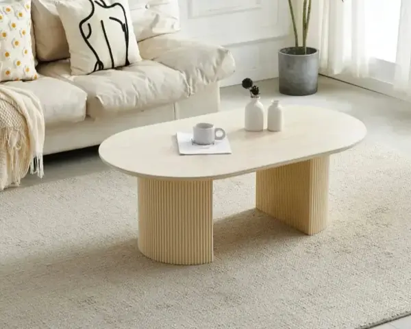 Table basse ovale avec pieds cannelés, sur un tapis doux. Quelle déco avec du travertin, une tasse et des vases sur la table.
