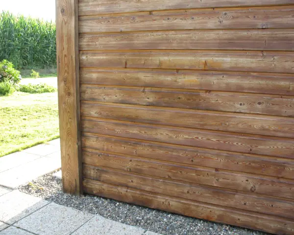 Bardage en bois de mélèze, traité pour l'extérieur, avec un poteau vertical. Le bois présente des nœuds et un grain prononcé.