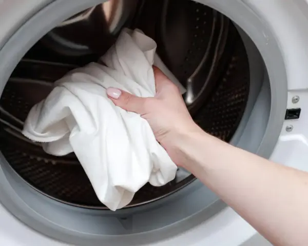 Main tenant met une serviette blanche dans le tambour d'une machine à laver pour dissoudre lessive durcie.