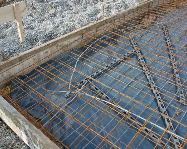 Préparation pour couler une dalle béton : film plastique, treillis métallique et coffrage en bois. On ne coule pas une dalle béton directement sur la terre.