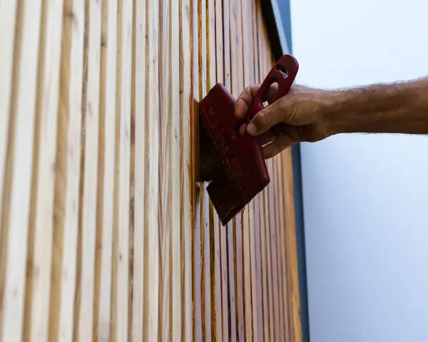 Maintenir son bois en parfait état : une main applique une huile protectrice sur des lattes de bois, comme pour fabriquer son huile de teck.